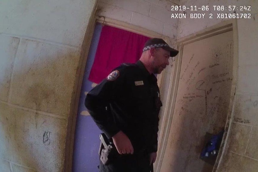 A NT Police officer can be seen in a screenshot from body-worn video. The officer is knocking on a door.