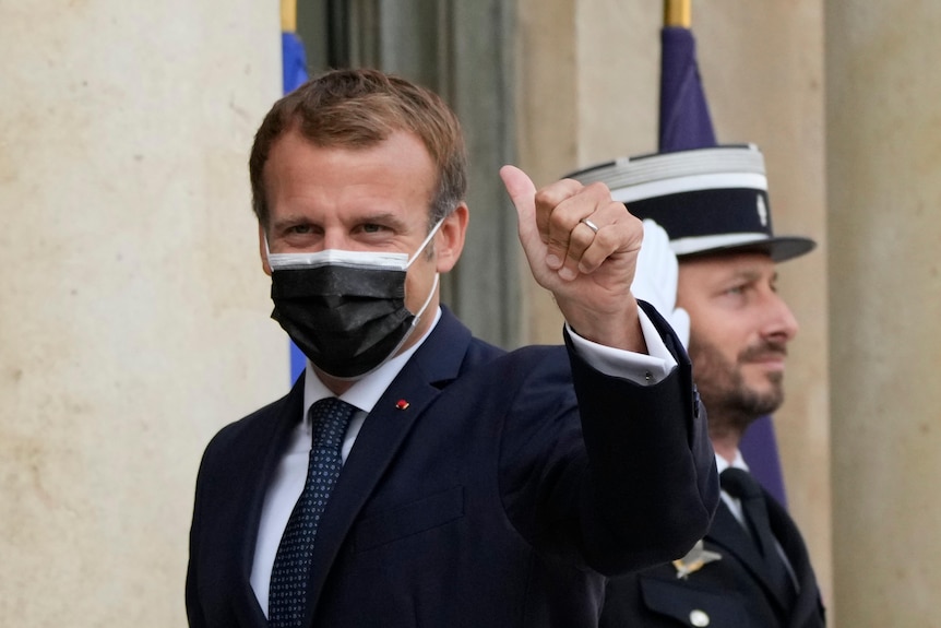 Președintele francez Emmanuel Macron arată cu degetul mare în sus în timp ce poartă o mască