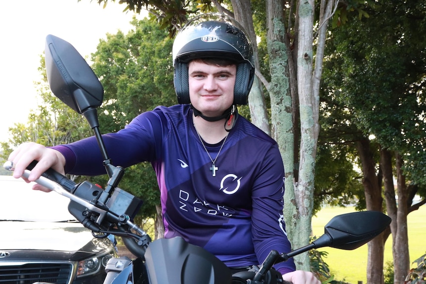 A young man wearing a helmet while reading a motorcycle.