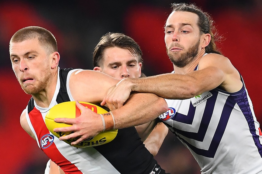 A St Kilda AFL player holds the ball as he is tackled by Fremantle opponent.