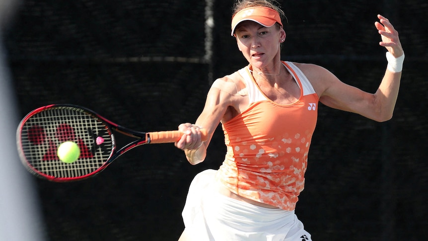A woman in an orange tennis outfit hits a green ball.