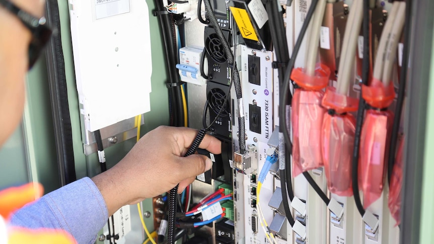 Close up of workman's hands installing NBN fibre to a node box.