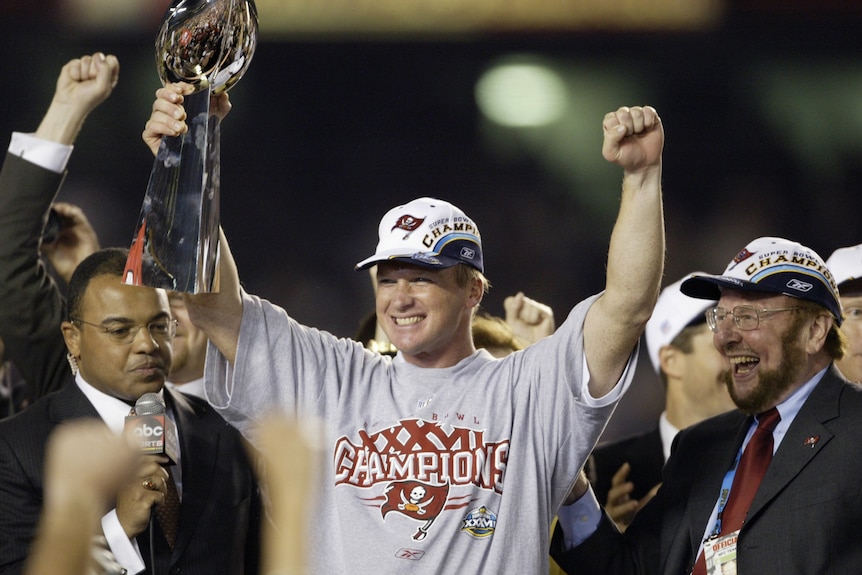 An NFL coach smiles as he holds the Super Bowl trophy with his right hand in 2003.