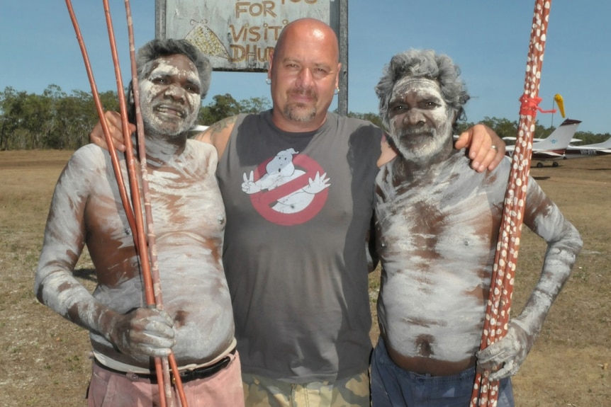 Wayne stands in the middle of two men holding spears