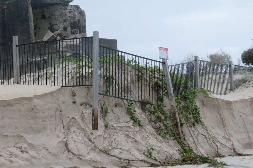 Fence falling down eroded sand dune with concrete bunker in background.