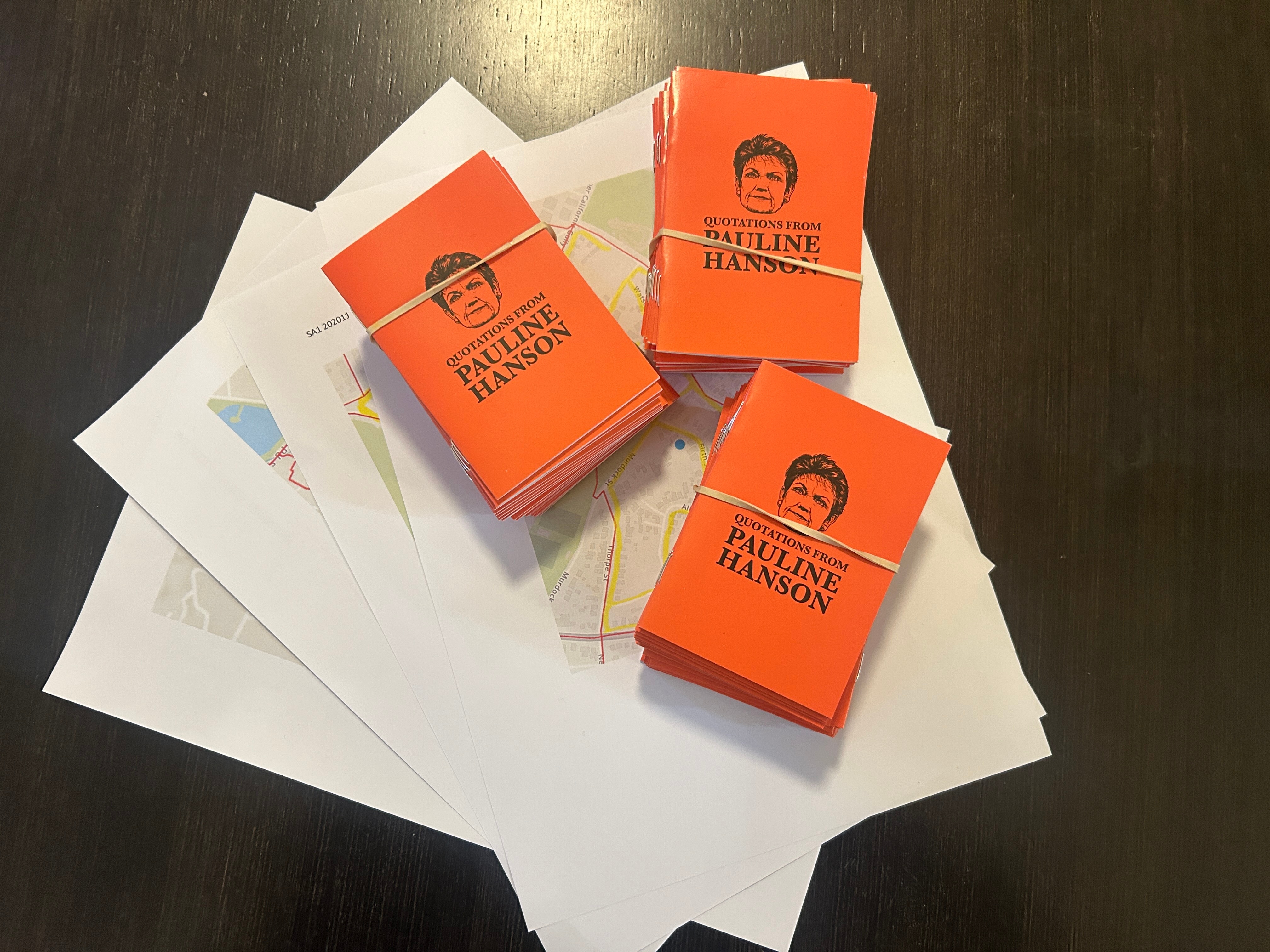 Bundles of orange booklets with Pauline Hanson's face sitting on a table.