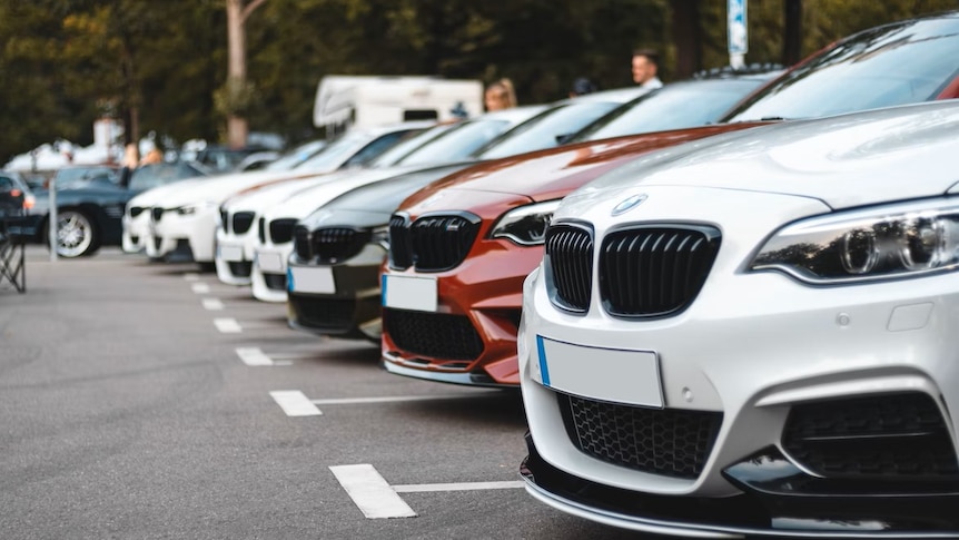 A row of about seven new-looking cars reversed into car parks in a line next to each other.