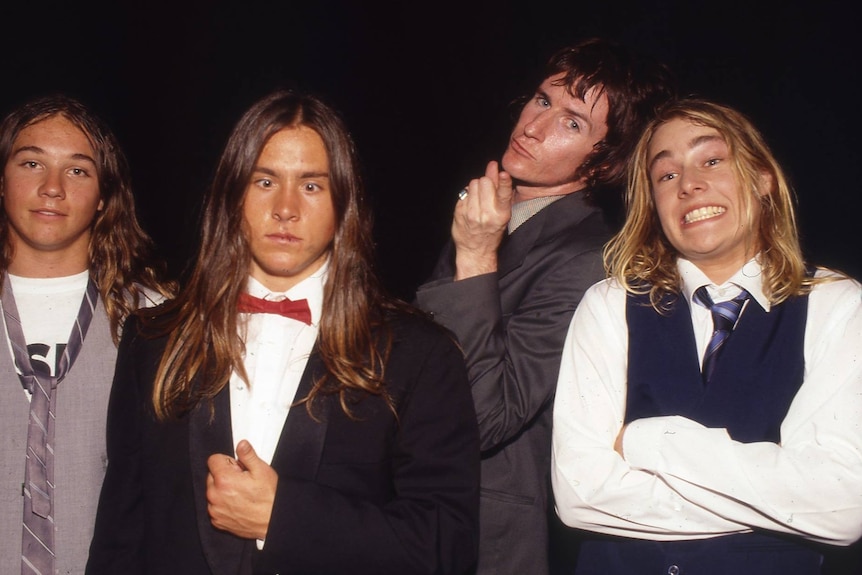 Four young men, three with long hair, clowning for the camera.