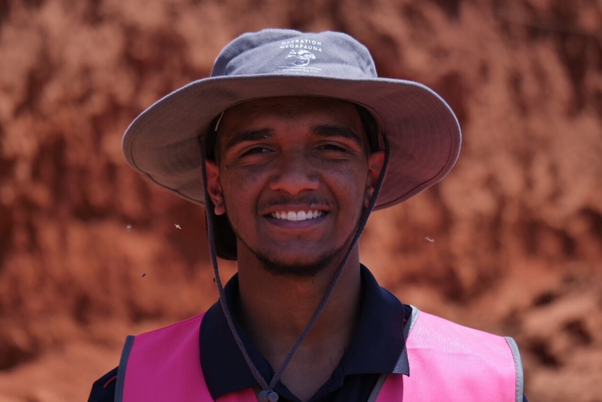 Young boy smiles in hat in front of red cliff 