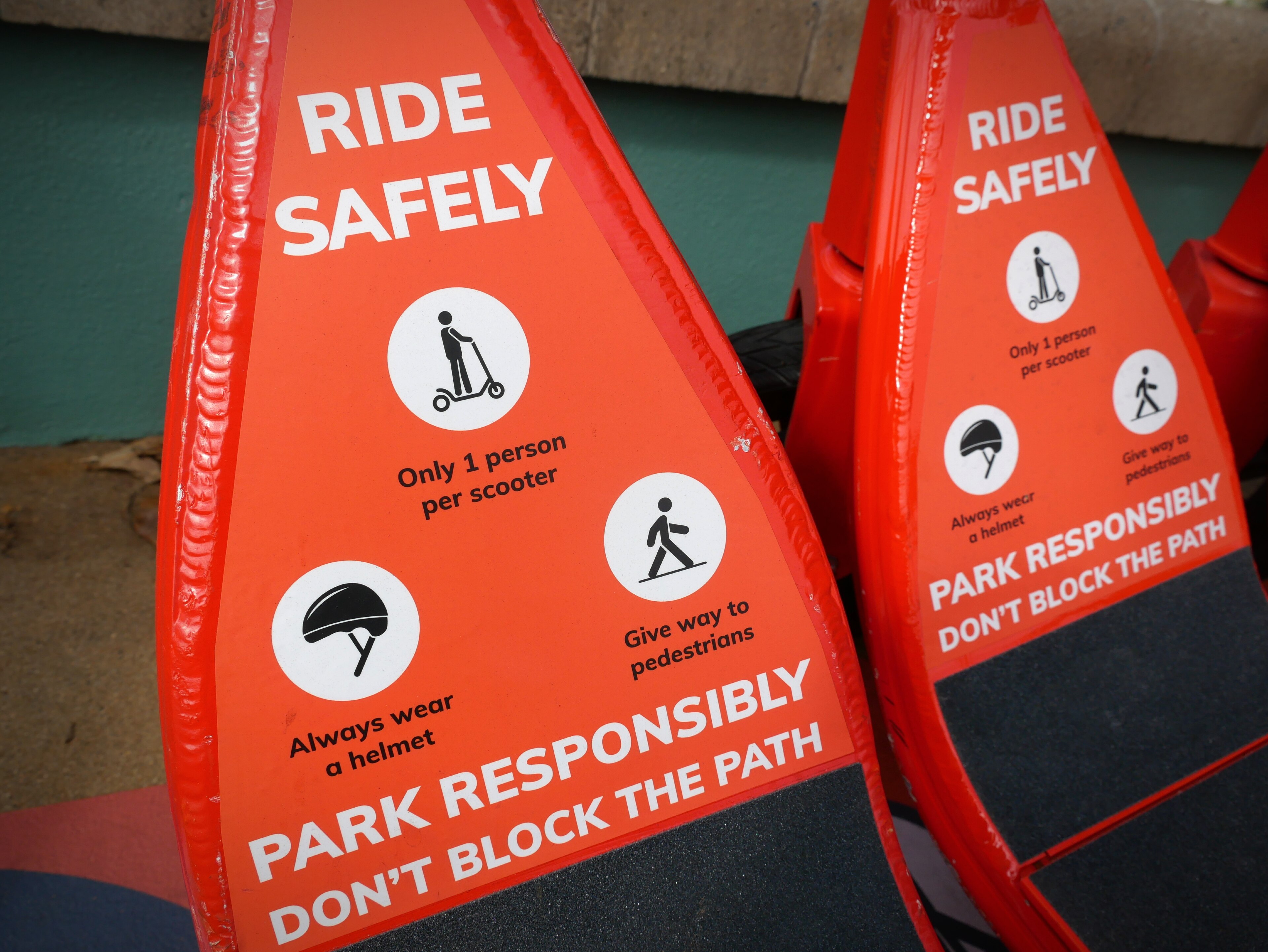 Close up of red safety sign on e-scooter saying ride safely, park responsibly, don't block path, with figures depicting action.