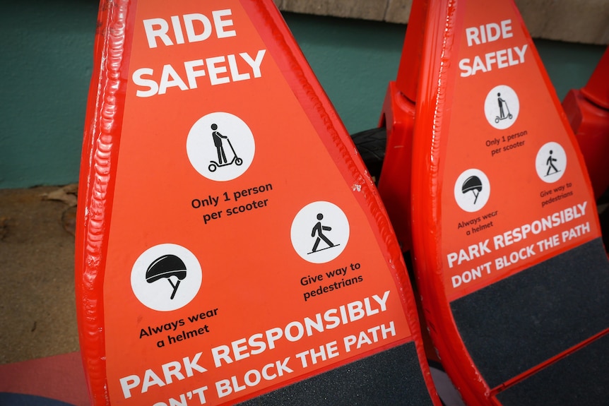 Close up of red safety sign on e-scooter saying ride safely, park responsibly, don't block path, with figures depicting action.
