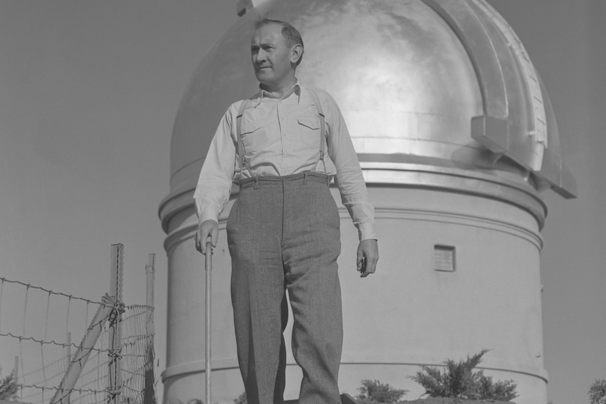 A black and white picture of a man standing in front of a large telscope.