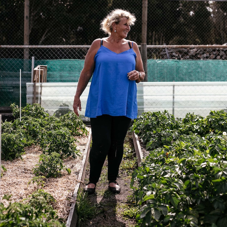 a woman stands in between two beds of vegetables