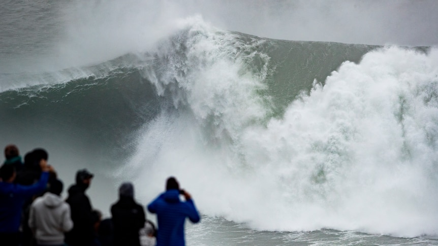 Spectators watch from a cliff as waves churn together below them