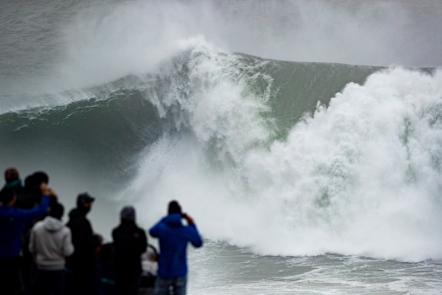 Spectators watch from a cliff as waves churn together below them