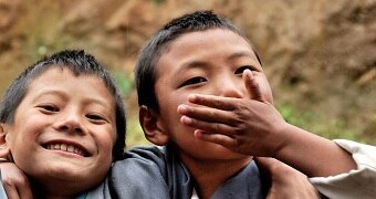 One boy, who is smiling, is standing next to another boy who has one hand over his mouth.