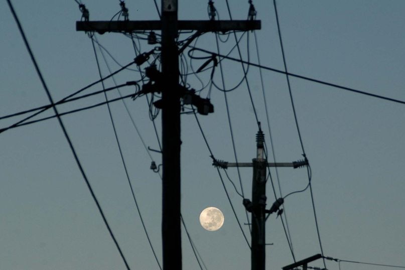 The full moon rises through powerlines