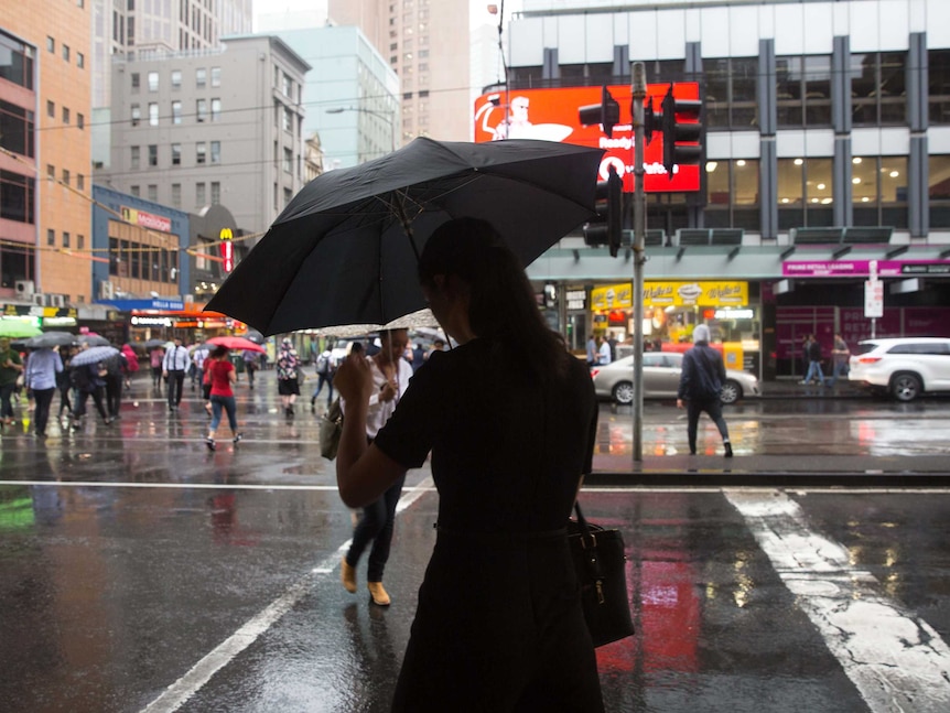 Pedestrians cross the road in rain at corner of Flinders and Elizabeth Streets.