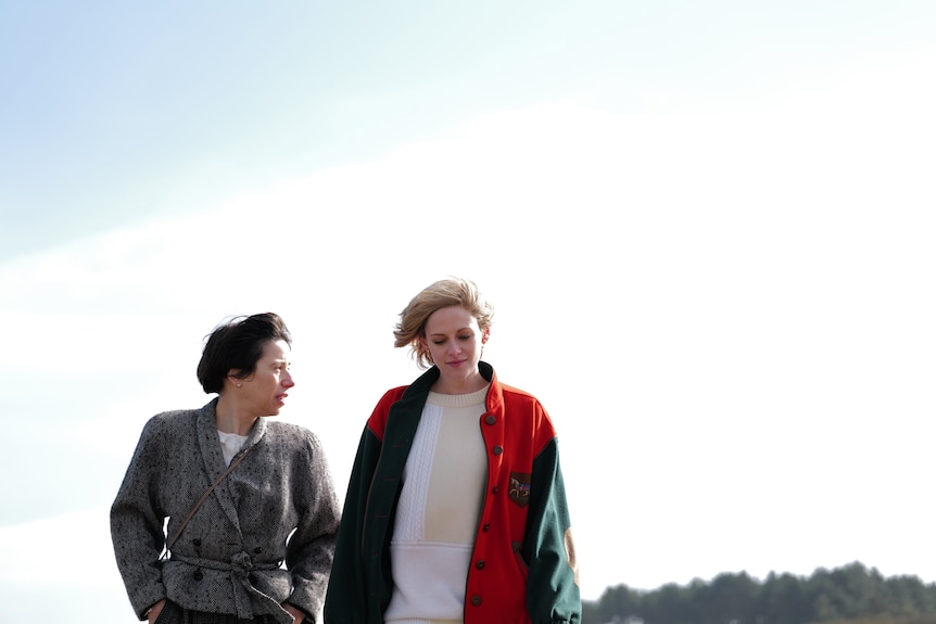 A 40-something woman and a 30-something woman, wearing winter coats and jackets, talk as they walk outside together