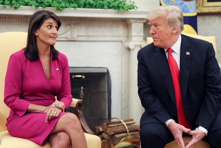 A woman in a pink dress sits next to former president Donald Trump. The pair are looking at each other.