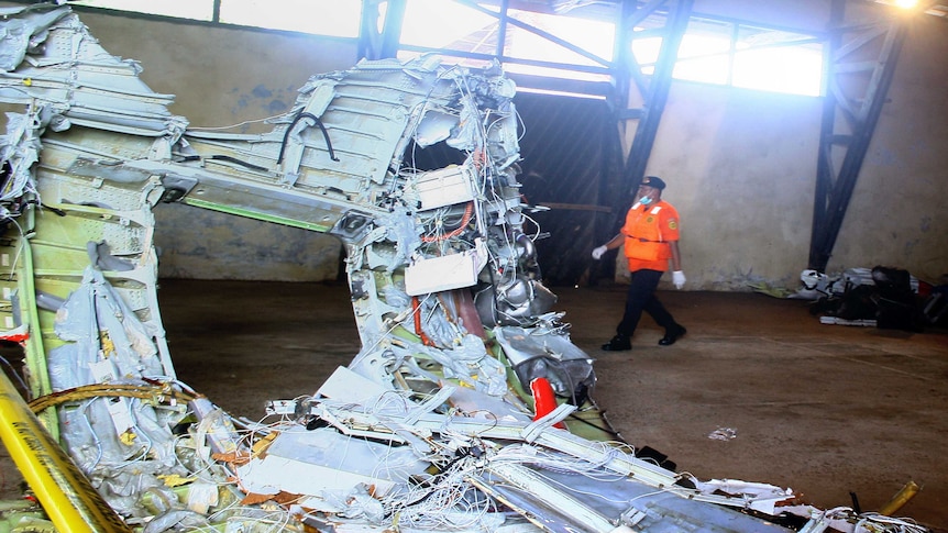 A member of Indonesia's search and rescue team walks past a piece of the plane wreckage.