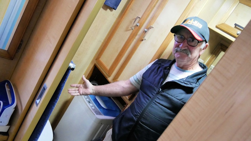 Gary in the bathroom of his caravan, pointing towards toilet