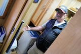 Gary in the bathroom of his caravan, pointing towards toilet