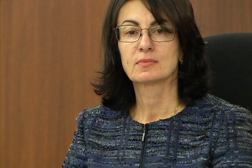 A woman in a blue top and glasses sits in court in a judge's chair.
