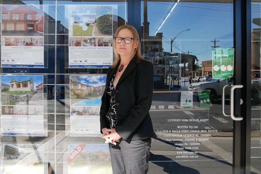 A female real estate agent stands outside her office.