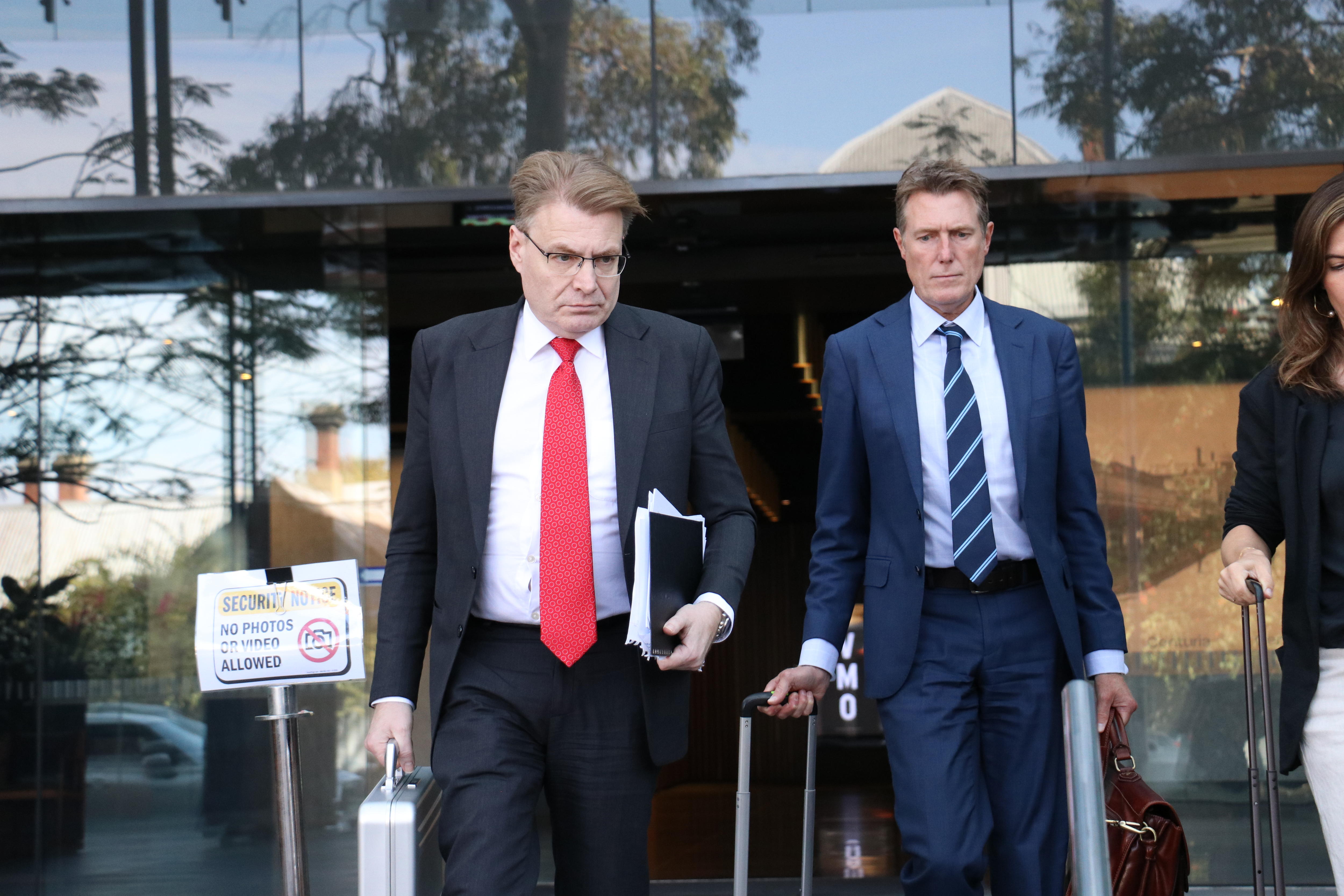 Two men in suits walk out of a glass door.