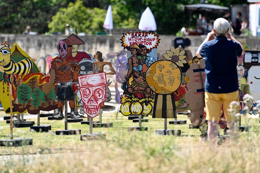 An installation of colourful painted cardboard cut-outs on a grass lawn, with a person taking a photo.