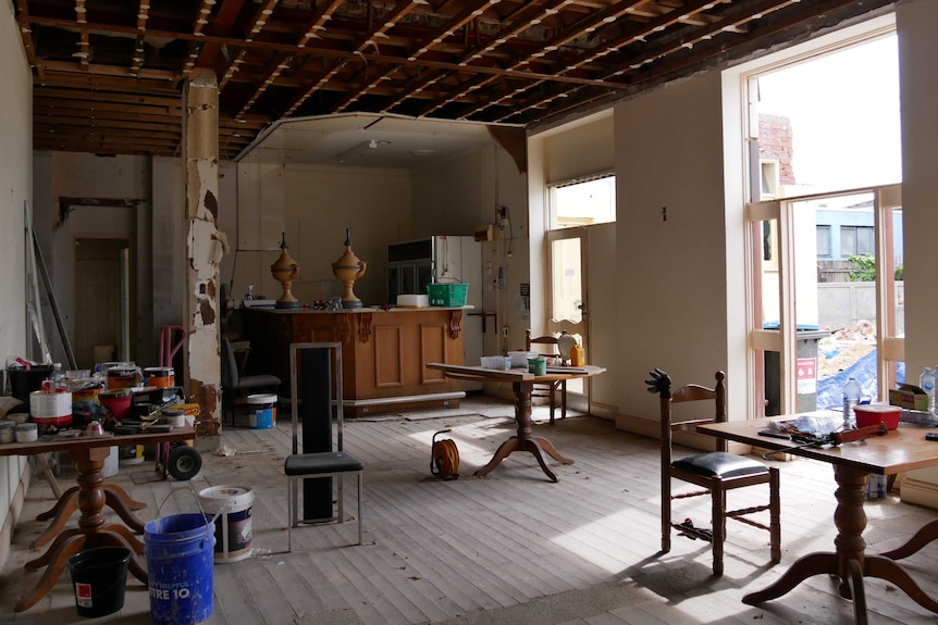 A room is deconstructed with an exposed roof. Tools and paint lie around the room.
