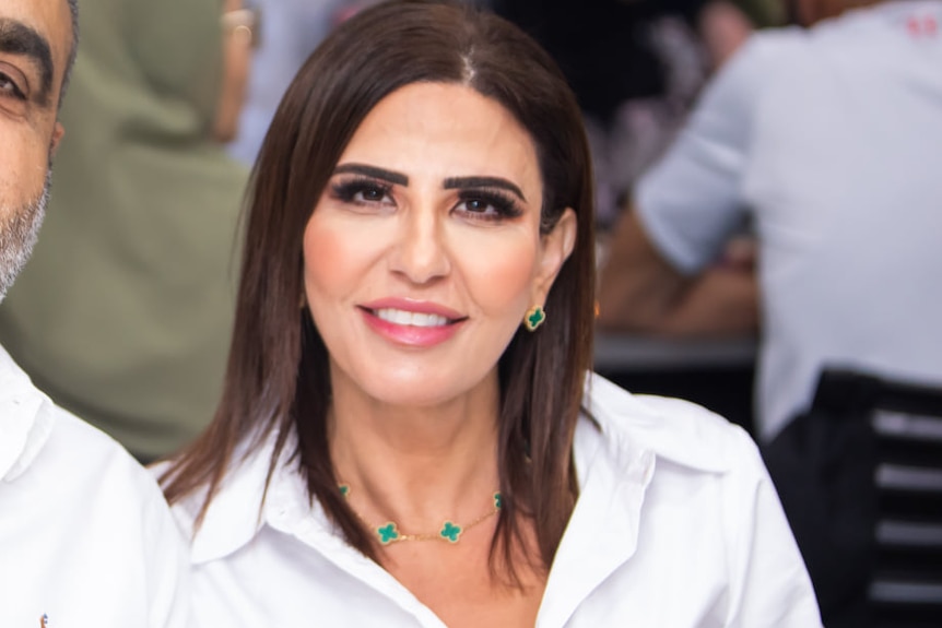 A woman wearing earrings, makeup and a white shirt smiles to the camera