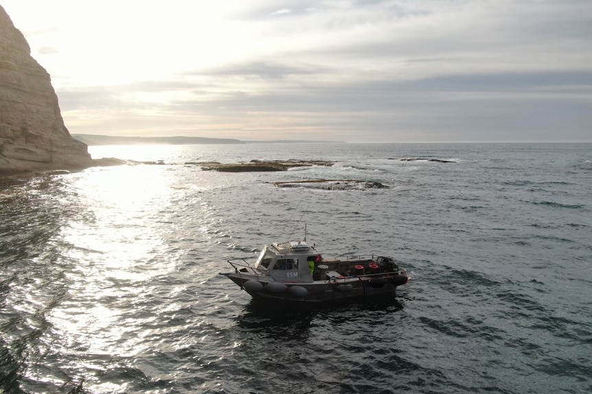 Aerial photo of boat in the water off a coastline with cliffs.