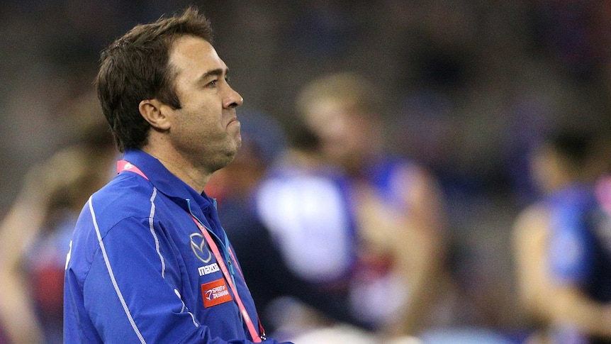 Brad Scott watches the Kangaroos play the Bulldogs from the sidelines while holding pieces of paper.