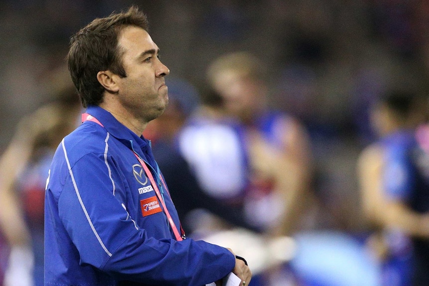 Brad Scott watches the Kangaroos play the Bulldogs from the sidelines while holding pieces of paper.