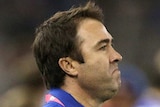 Brad Scott watches the Kangaroos play the Bulldogs from the sidelines while holding pieces of paper.