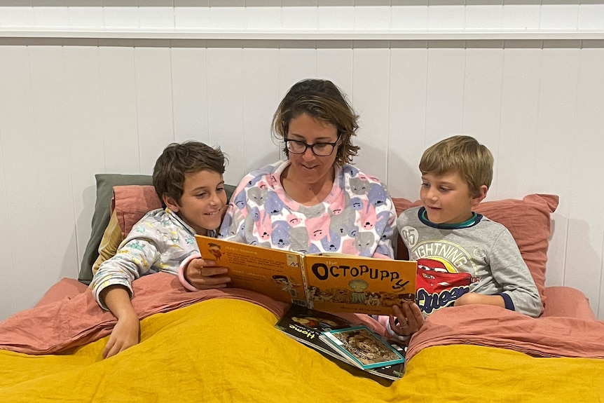 A woman sits between two young boys reading them a storybook.