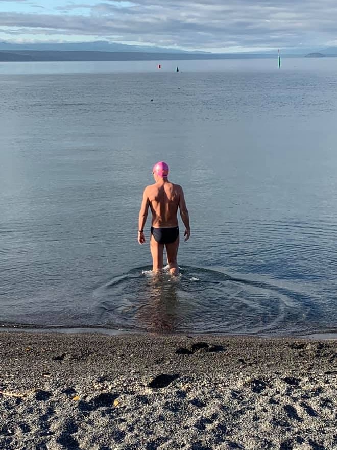 Swimmer Michael Wells in trunks walking into the water of Lake Taupo in New Zealand