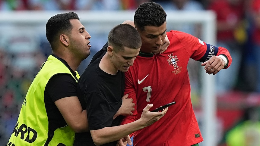 A security guard tries to grab a pitch invader, who has grabbed onto Cristiano Ronaldo