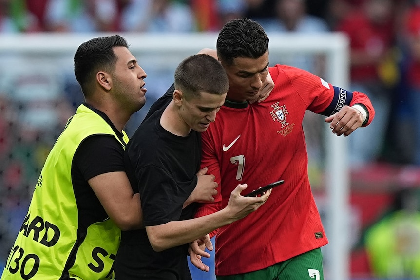 A security guard tries to grab a pitch invader, who has grabbed onto Cristiano Ronaldo