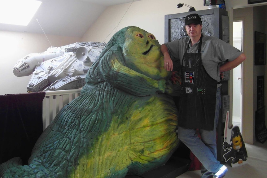 A man leans on a model of a large slug-like creature with a face