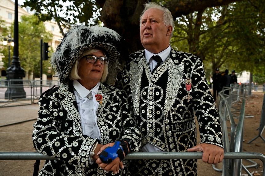 A man and woman in black sequined outfits stand at a barricade.