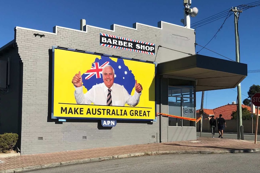 A grey suburban building with a bright yellow sign saying Make Australia Great, with a photo of Clive Palmer and flag.