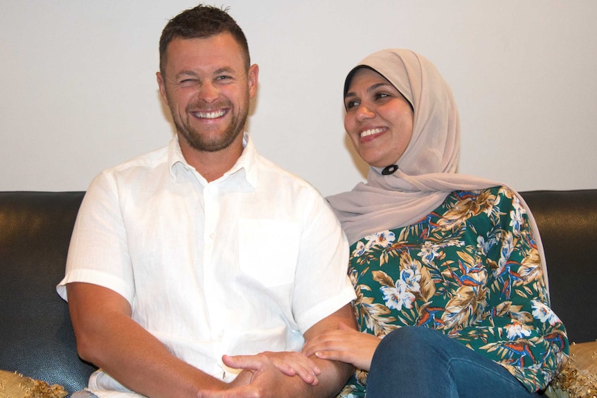 A man and a woman in a hijab sit side-by-side on a lounge, laughing together.