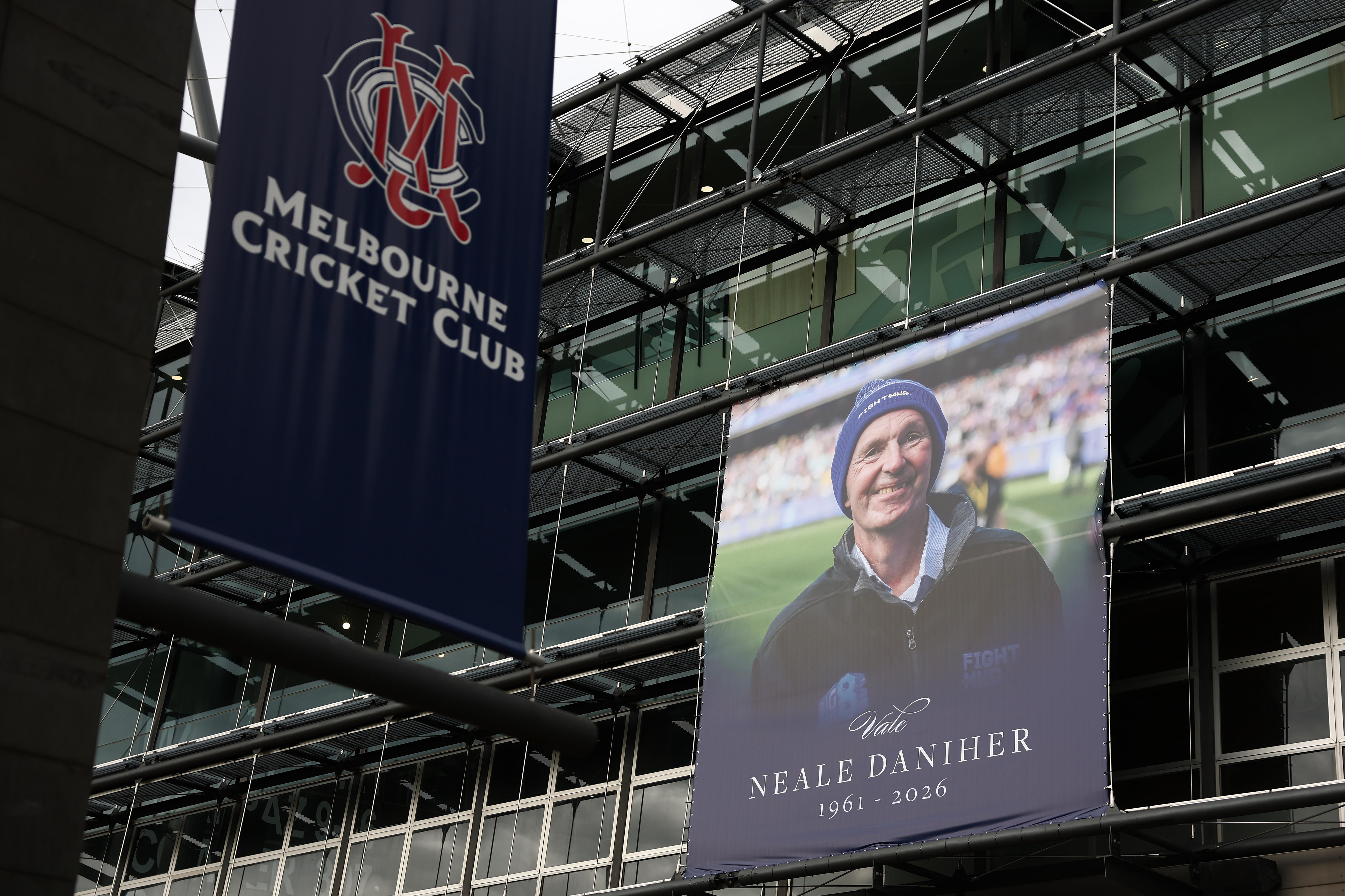 A billboard on the outside of a sports stadium showing a smiling man wearing a blue beanie and the words "Neale Daniher".