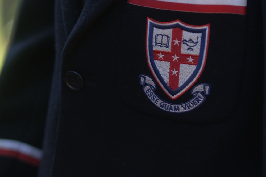 A close-up of a blue blazer with a school badge and the motto 'ESSE QUAM VIDERI'.
