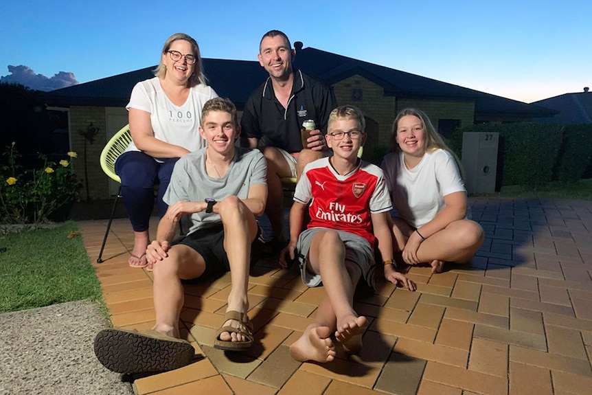 The Gehrke family - mum, dad and three teenagers, sit in the driveway of their home.