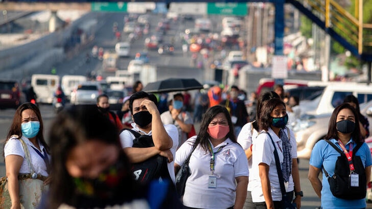 Dozens of workers wearing protective masks pictured standing on the road in Manila, Philippines.