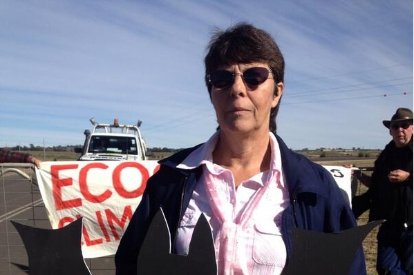 A woman with sunglasses holding a prop at a protest in front of a banner.